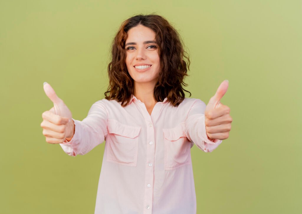 smiling young caucasian girl thumbs up with two hands isolated on green background with copy space